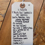 A white paper hangtag with handwritten text listing wine ingredients and descriptions, tied with a white string and placed on a wooden surface.