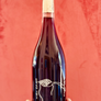 A bottle of High Camp Pinot Noir wine held in a hand, with a label featuring a dragonfly graphic.