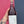 Hand holding a bottle of red wine against a pink and blue wall.