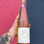 Bottle of rosé wine held by a person with a tattooed arm against a pink and blue background