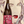 A bottle of Camins 2 Dreams Carbonic Carignan wine with a colorful label, held in front of a painted portrait of a woman with red lips.