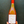 Bottle of orange wine with a red cap held against a dark background