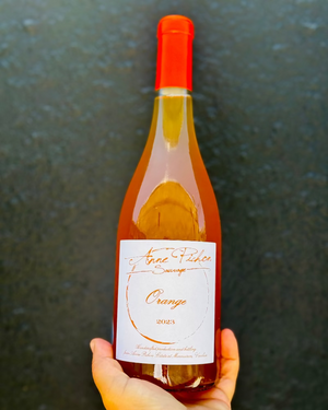 Bottle of orange wine with a red cap held against a dark background