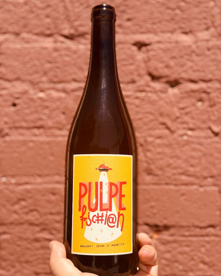 Bottle of Pulpe fashion with a yellow label against a brick wall.