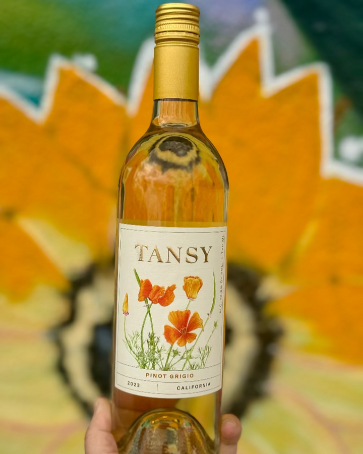 Bottle of Tansy wine with a floral label against a blurred natural background