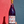 Bottle of red wine with a decorative label held against a red and blue wall.