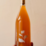Hand holding a bottle of amber liquid with a cork, against a beige background