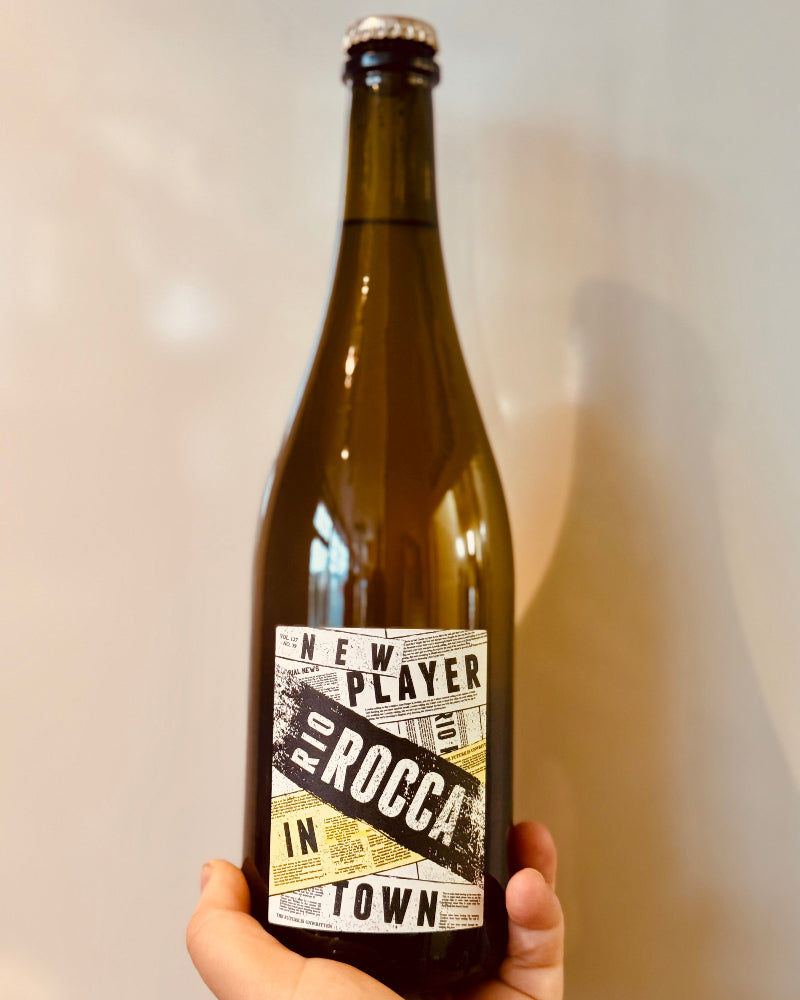 Bottle of New Player Rio Rocca with a label held by a hand against a neutral background