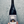 A hand holds a dark glass wine bottle with a white label featuring a black-and-white architectural photograph and the handwritten text 'Woman, diest fragte?'. The background is a textured gray wall.