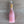 A small pink bottle-shaped candle with a gold neck and white wick, lying on a brown wooden surface.