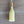 A novelty bottle-shaped candle in pale yellow wax with a metallic gold neck and a white wick, placed on a brown wooden surface.