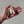 A hand holding three small fishing lures, including a dark glittery topwater, a pale yellow skirted lure, and a dark green skirted lure, against a neutral concrete background.
