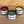 Three black soy candles in round black jars on a wooden surface, labeled Sapphoir Faire: VIVA LA VULVA, ABUNDANCE, and QUEER JOY, with red, green, and yellow wax visible.