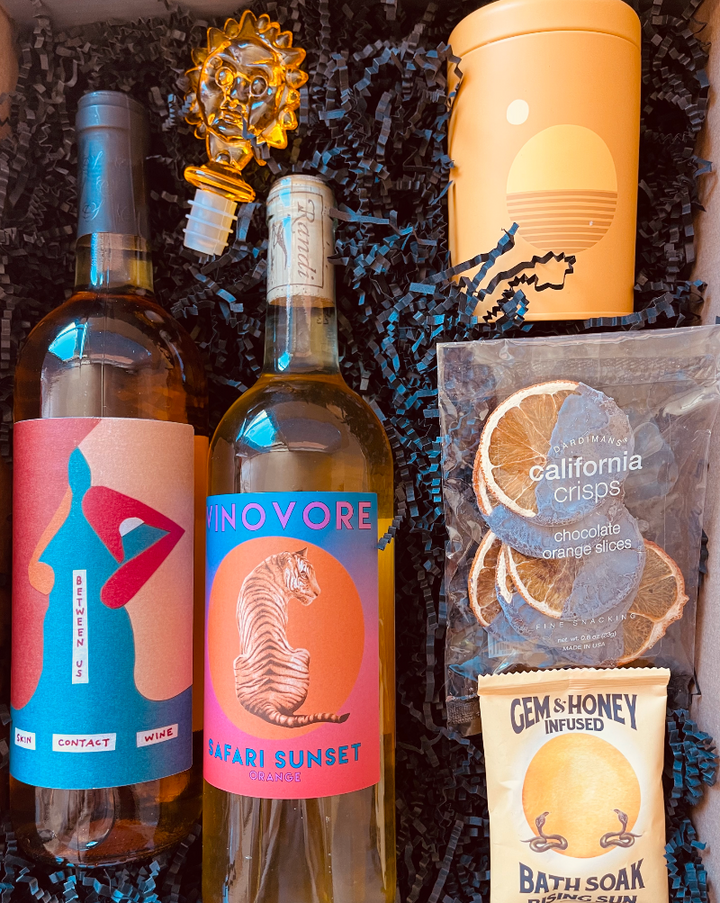 This box includes Vinovore Between Us wine, Vinovore Safari Sunset wine, P. F. Candle Co. Golden Hour candle, Crispy Dark Chocolate Orange Slices, Wild Yonder Botanical Bath Salts & Body Scrub (choose your pack) and an Acrylic Wine Stopper (choose your color).