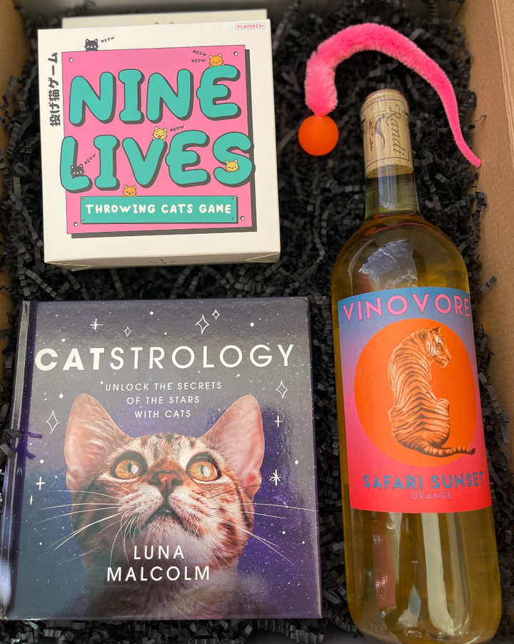 This box includes Vinovore Safari Sunset wine, Nine Lives Throwing Cats game, Catstrology book, and a cat toy (colors are assorted).