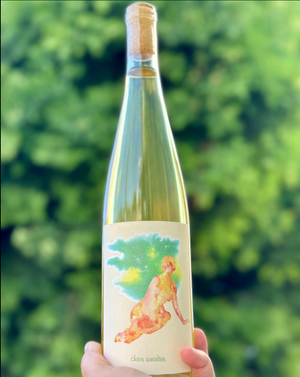 Wine bottle with a colorful label held against a blurred green background
