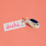 Fish-shaped hair clip with 'dashi' label on a pink background