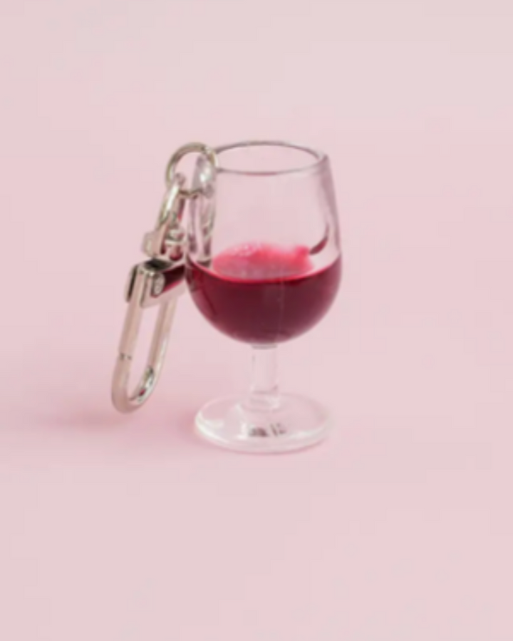 Keychain shaped like a wine glass with red liquid on a pink background