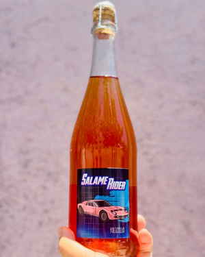 a hand holding a pink wine bottle with label that has a racecar on it against a blurry background
