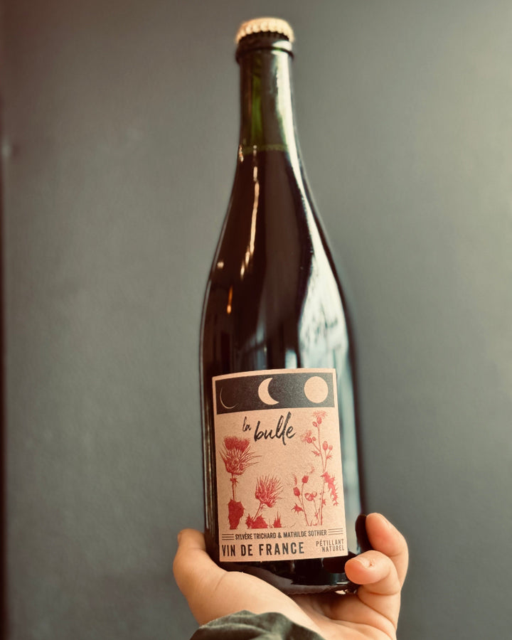 Bottle of wine held by a hand with a label on a gray background