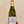 A hand holding a bottle of Vitteaut-Alberti Cremant de Bourgogne Blanc de Blancs sparkling wine against a textured beige wall.