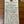 A handwritten cream-colored paper wine tag with a wooden hanging hole, placed on a brown wooden surface. The tag lists wine cellar details and flavor notes for a wine in Coteaux de Travers 'ZOUZOU' with varietals like Syrah, Grenache, and Mouvredhe, and notes 'ALL NATURAL' and 'CHILL OR NOT!'.