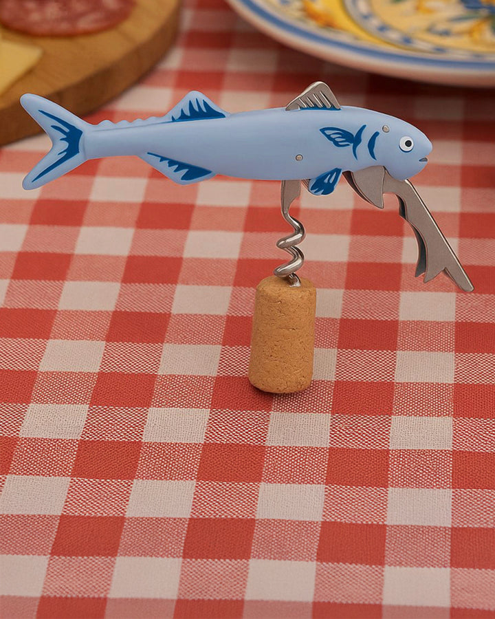 Shark-shaped bottle opener on a cork, placed on a red and white checkered tablecloth.